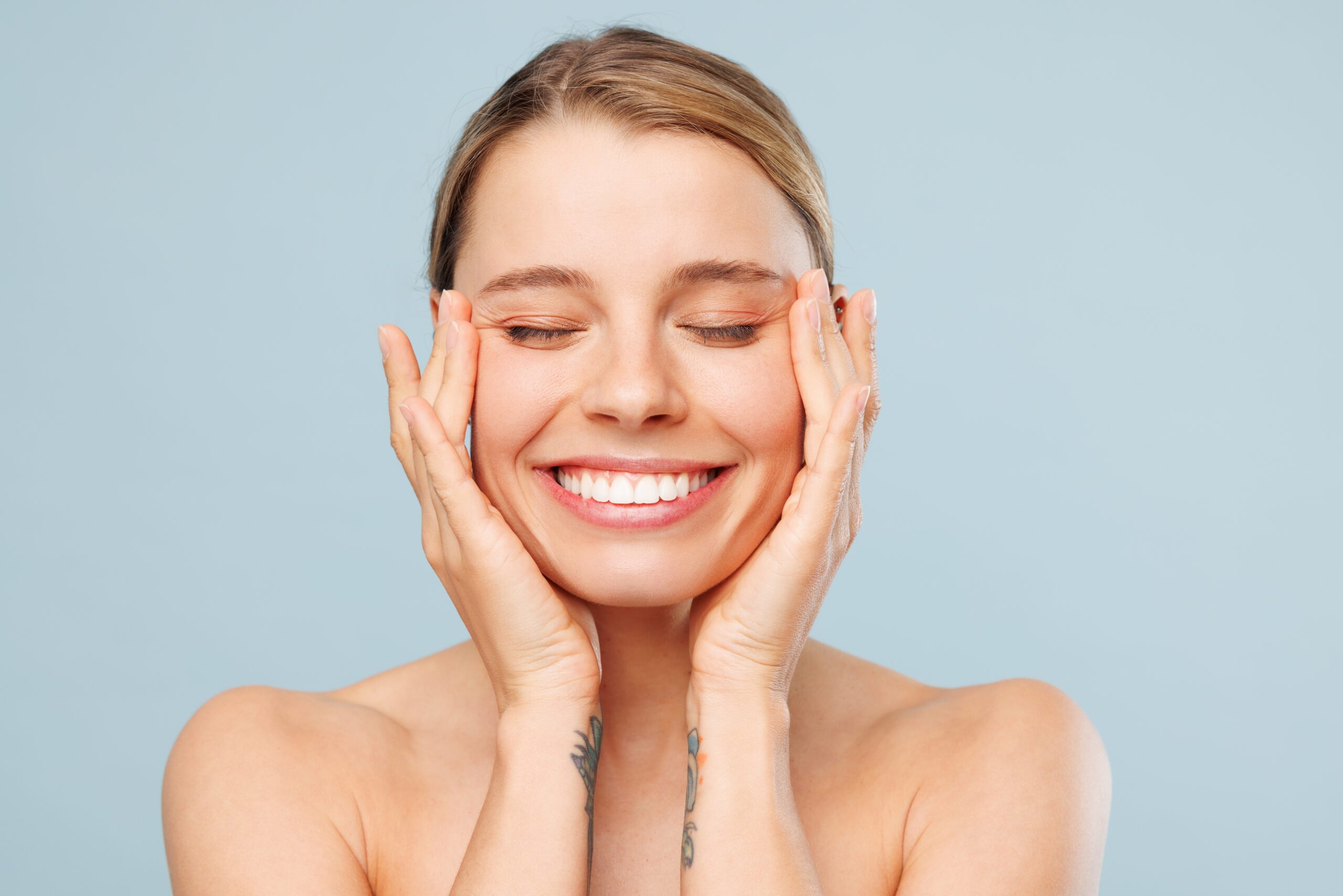 young woman smiling, showing her perfect smile against a light blue background