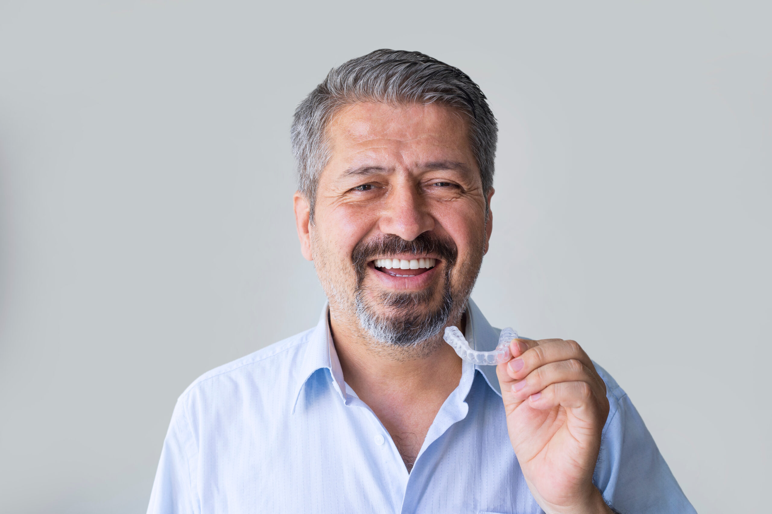 older man holding his clear aligners against a grey background