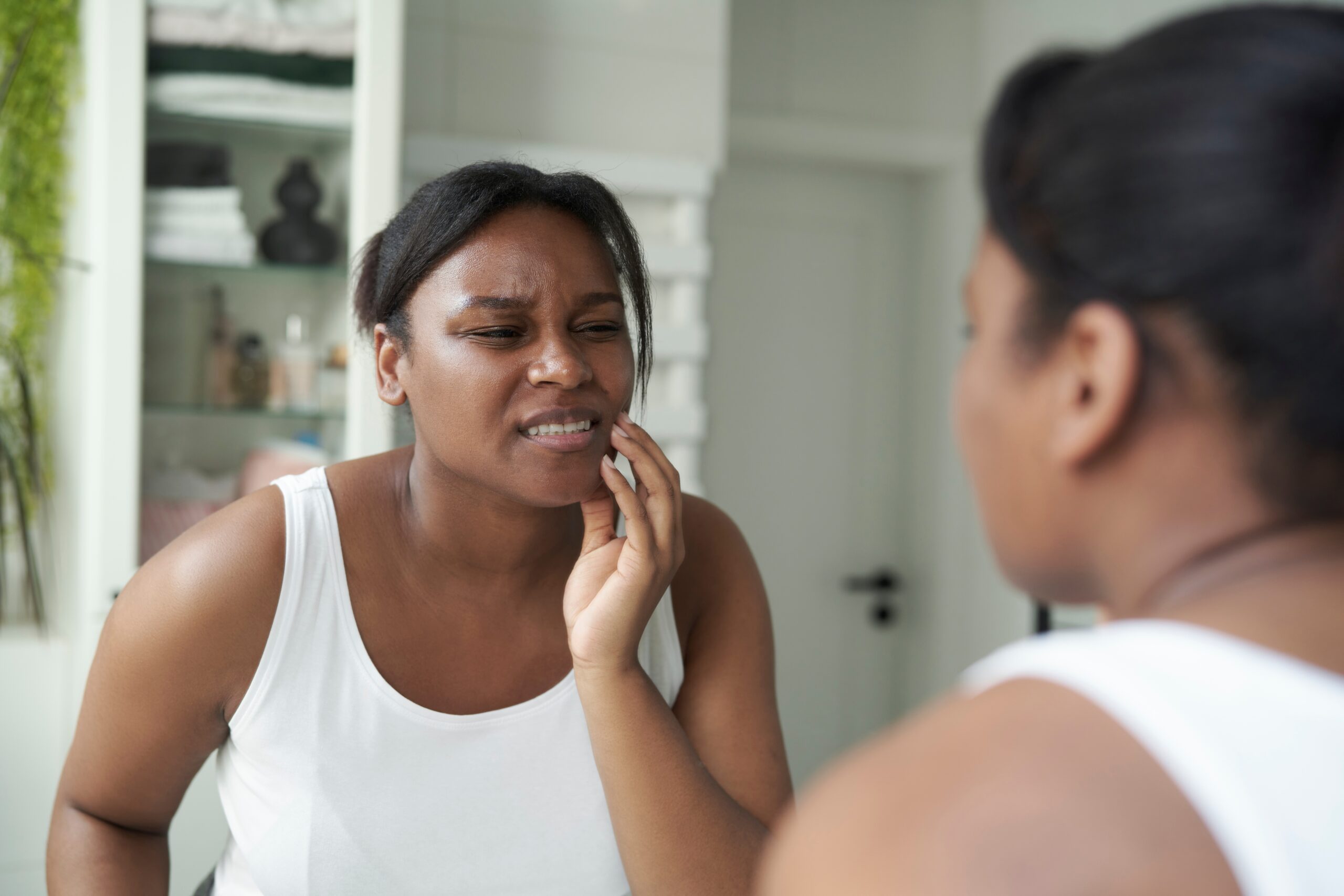 woman looking in mirror holding her jaw in pain