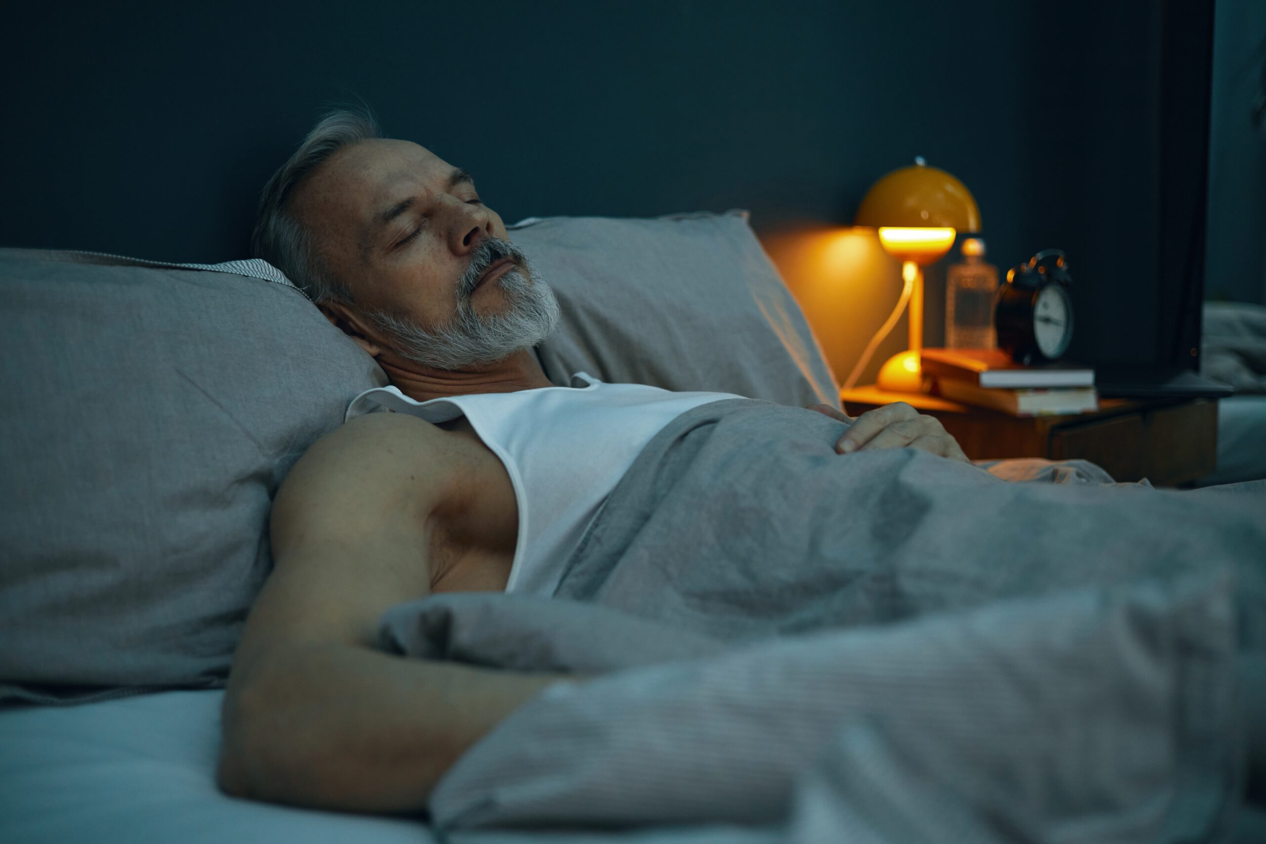 Elderly man peacefully sleeping in bed with warm lighting from bedside lamp illuminating