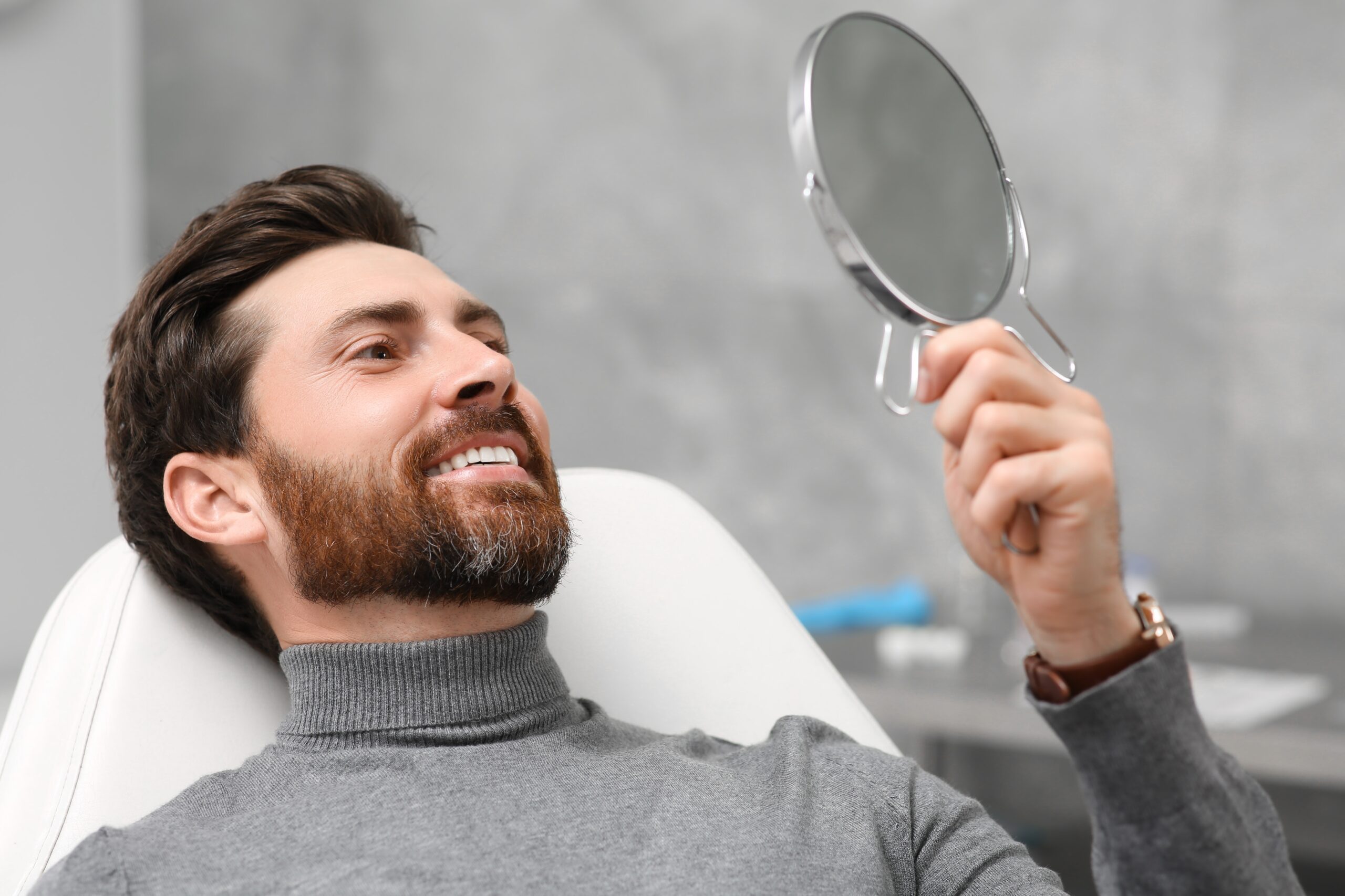 man smiling in the mirror, looking at new dental implants in office