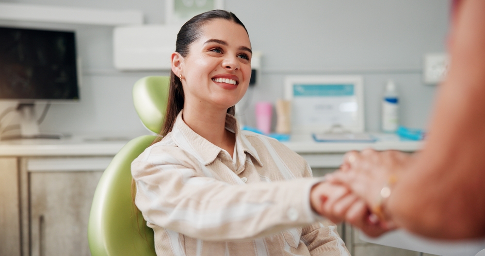 young woman smiling, holding hands with a dentist