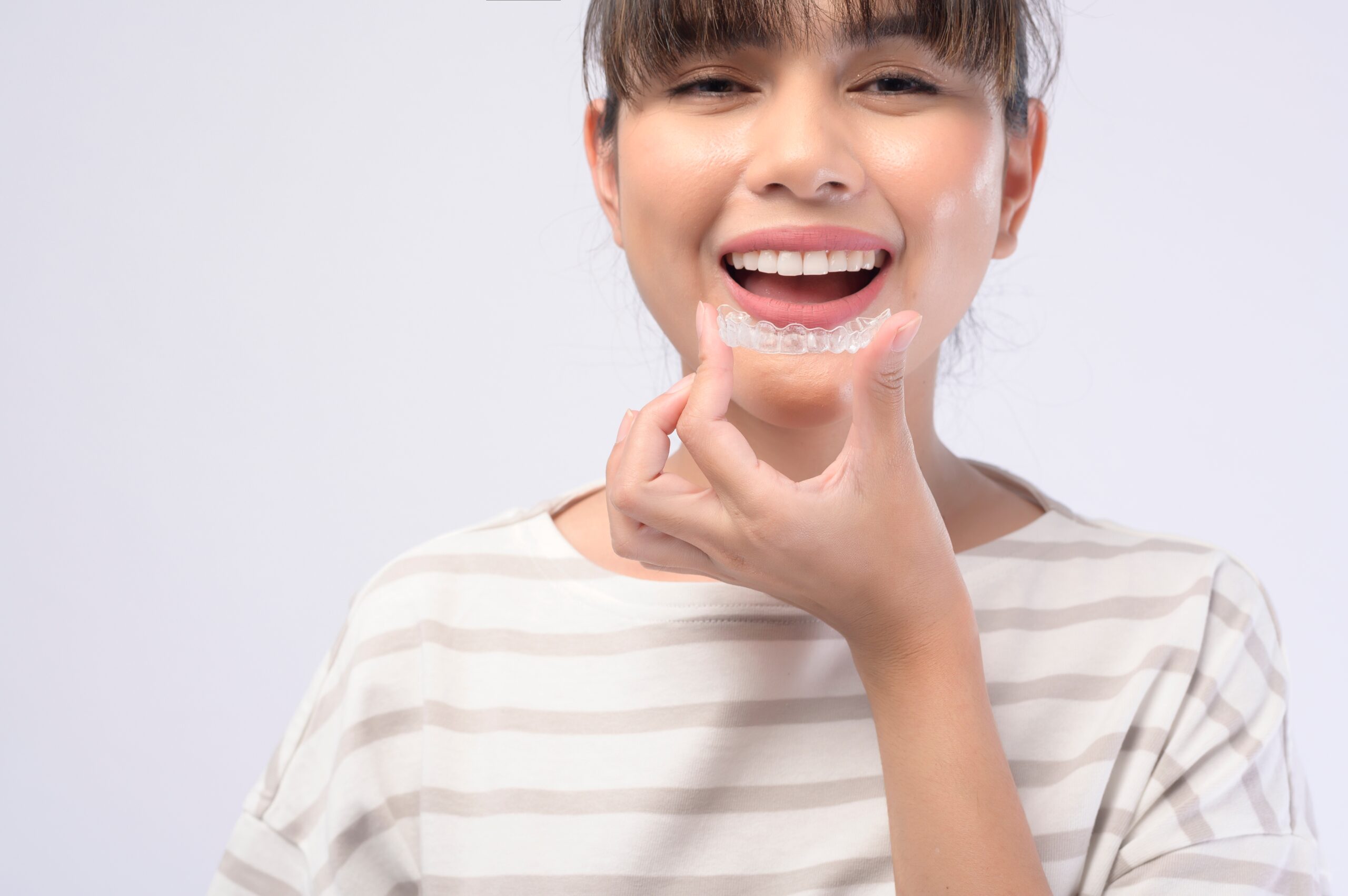 A smiling young woman holding clear aligners, white background