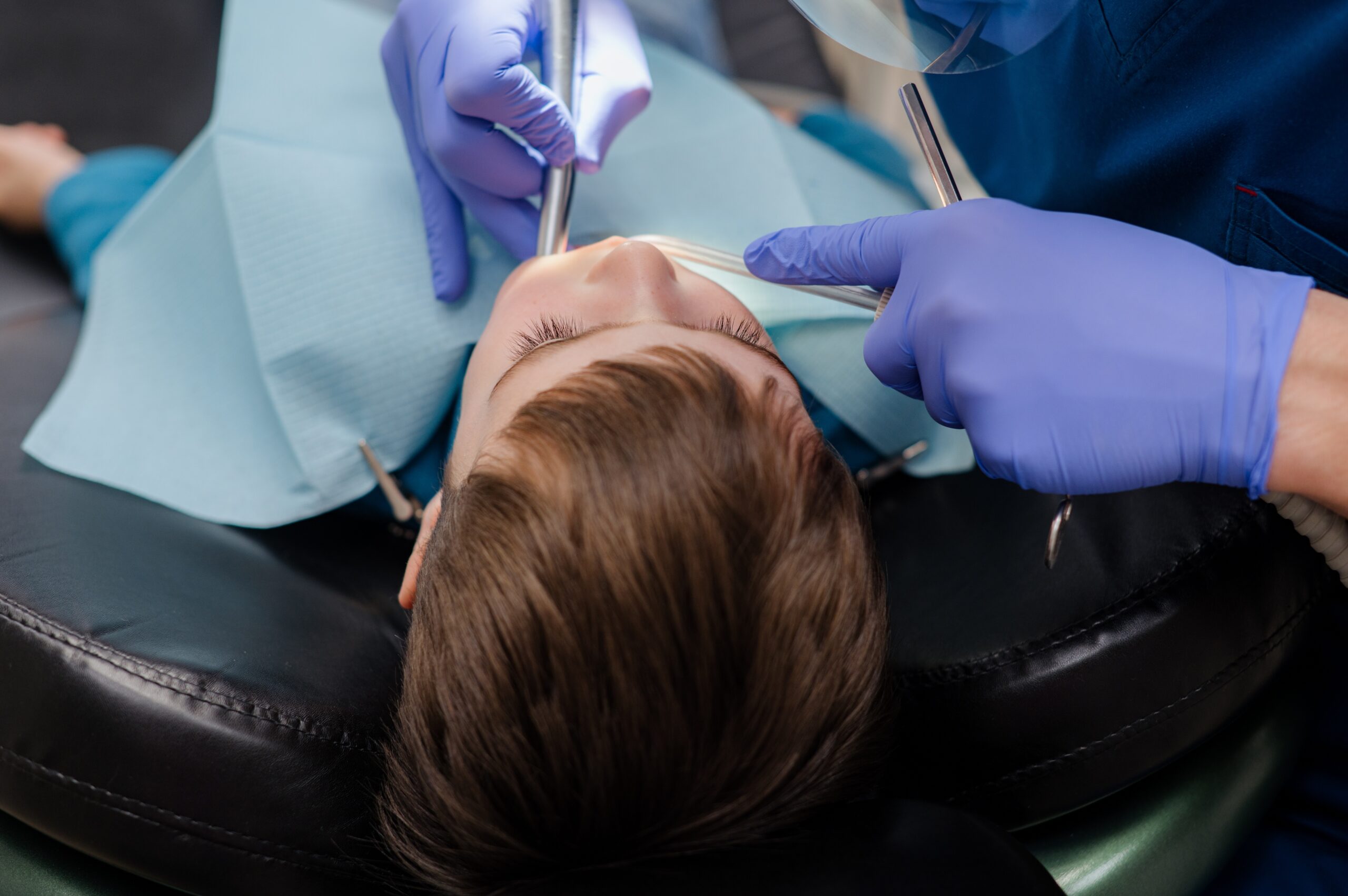 dentist in blue gloves checking young boys teeth